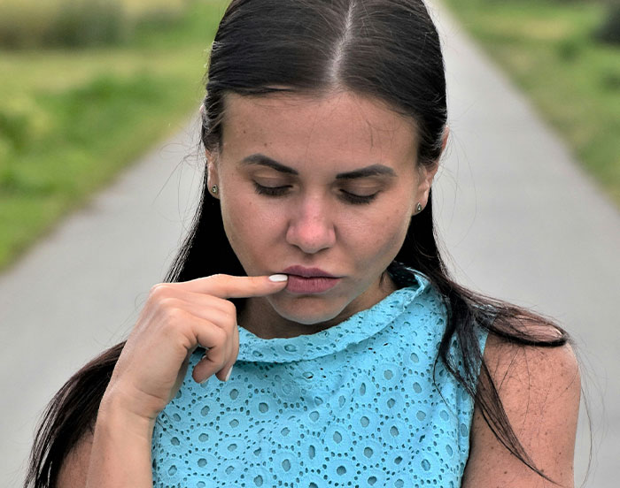 A woman in a blue dress looks down thoughtfully, showcasing attention-seeking behavior.