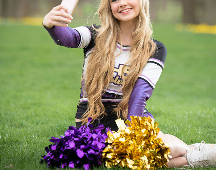 Cheerleader taking a selfie with pom-poms, showcasing actions for attention.