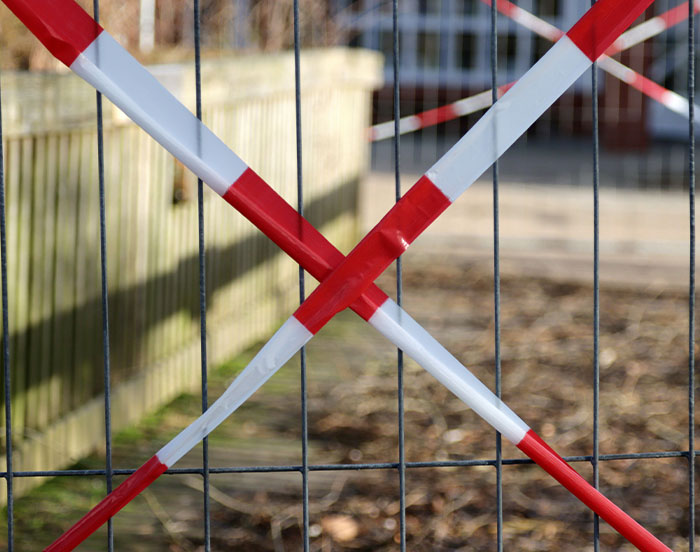 Red and white caution tape forming an X on a metal fence outside.