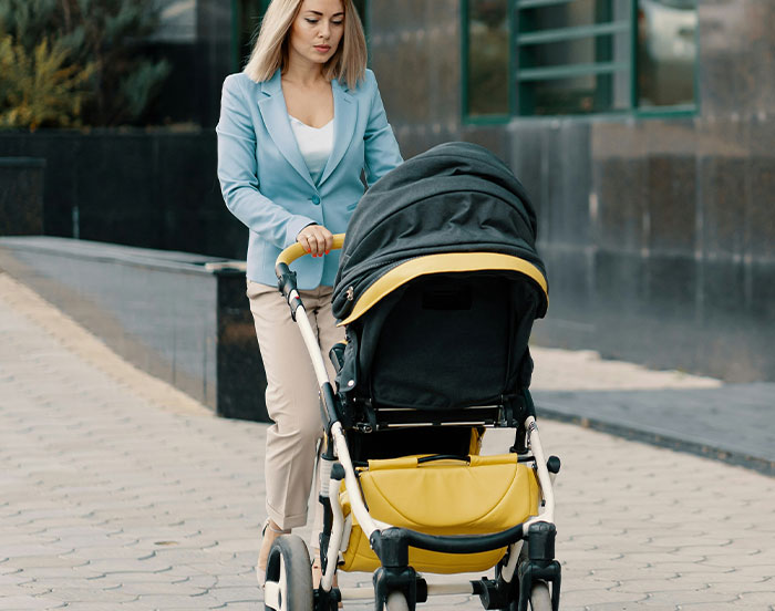 Woman in a blue blazer pushing a stroller on a sidewalk, related to unhinged attention-seeking actions.
