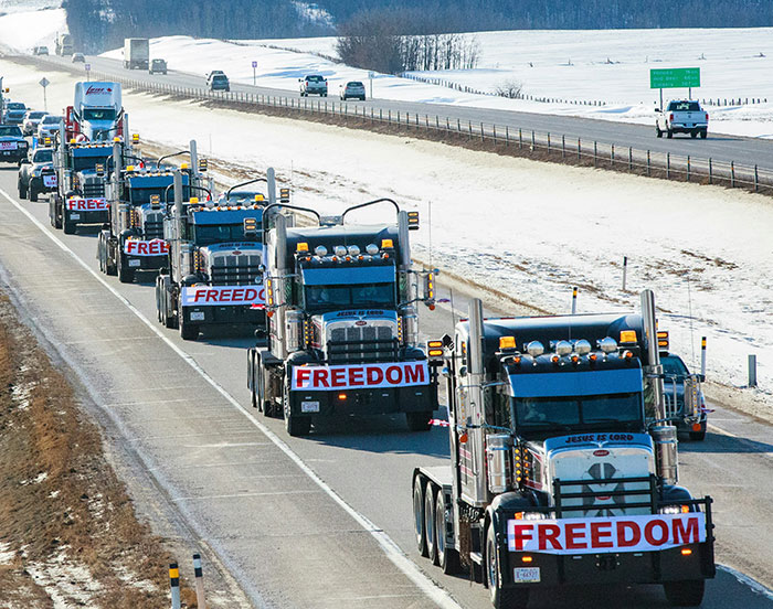 Convoy of trucks with "Freedom" signs, driving on a snowy highway for public attention.