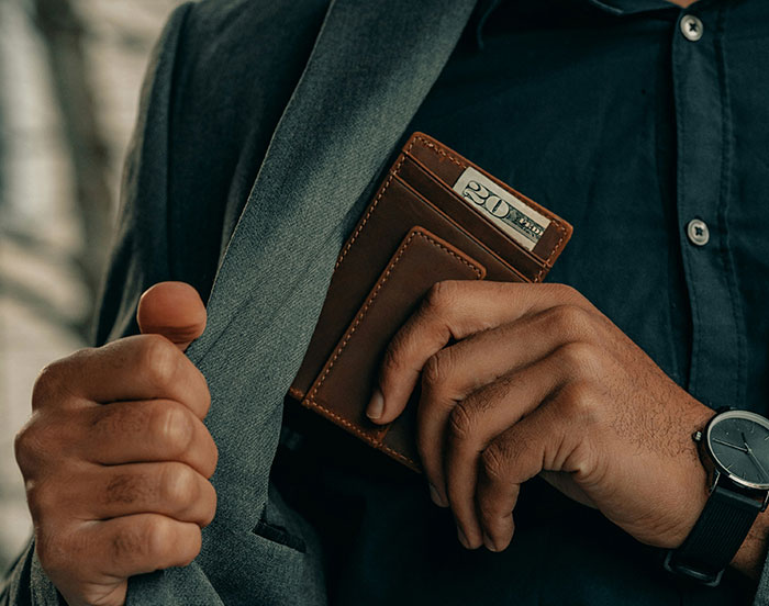 Man in suit holding a brown wallet with a twenty-dollar bill visibly inside.