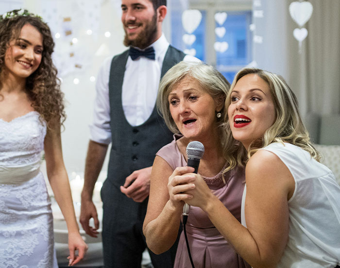 Guests at a wedding party singing into a microphone, capturing attention with joyful expressions.