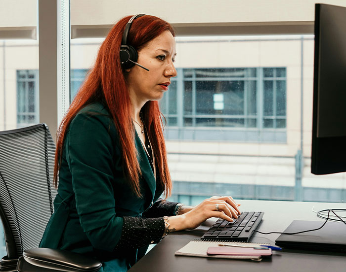 Office worker with headset at a desk, wearing a green jacket, typing on a keyboard; related to attention-seeking behavior.