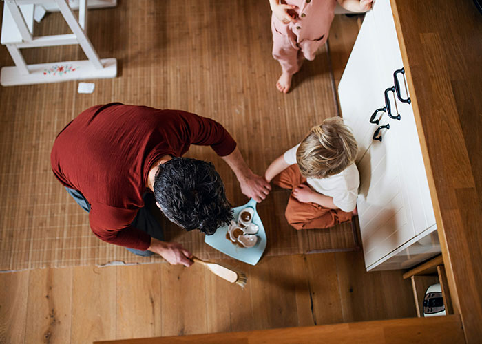 A man practicing gentle parenting, serving snacks to a child on a wooden floor.