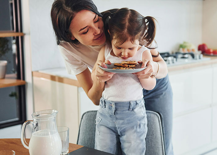 Mother and child in kitchen, practicing gentle parenting, holding a plate of cookies together.