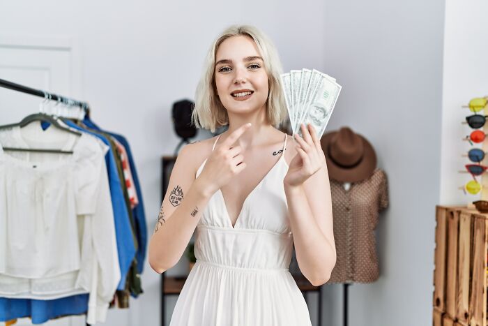 Person in a white dress holding cash, standing in a room with clothes, illustrating everyday people's habits.