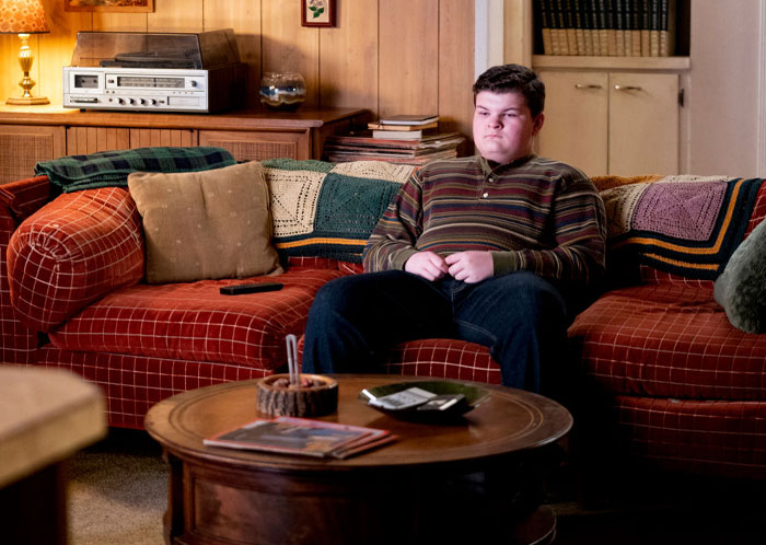 Young Sheldon cast member Wyatt McClure sitting on a vintage sofa in a cozy living room setting.