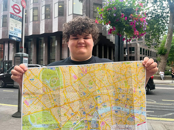 Young Sheldon cast member Wyatt McClure holding a city map on a street with buildings and flowers in the background.