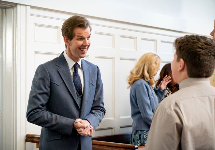 Matt Hobby in a suit smiling and talking to a young boy, with a group in the background. Young Sheldon cast interaction.