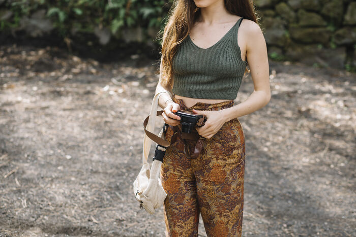 Woman in patterned pants holding a camera, showcasing recent fashion trends people hate.