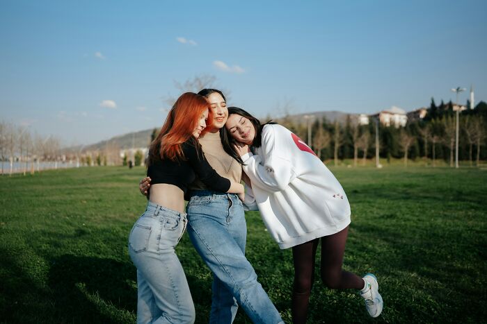 Three friends hugging in a park, embracing hardest harsh realities about life with smiles and support.