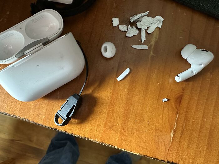 Broken earbud pieces and open charging case on a wooden table, illustrating someone's love for their device.