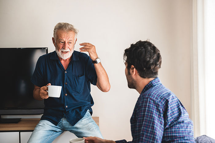An older man and a younger man discussing in a living room, focusing on cultural differences.