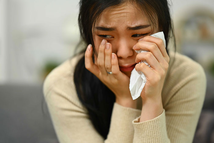 Thai wife feeling upset, holding tissue, facing family racism.