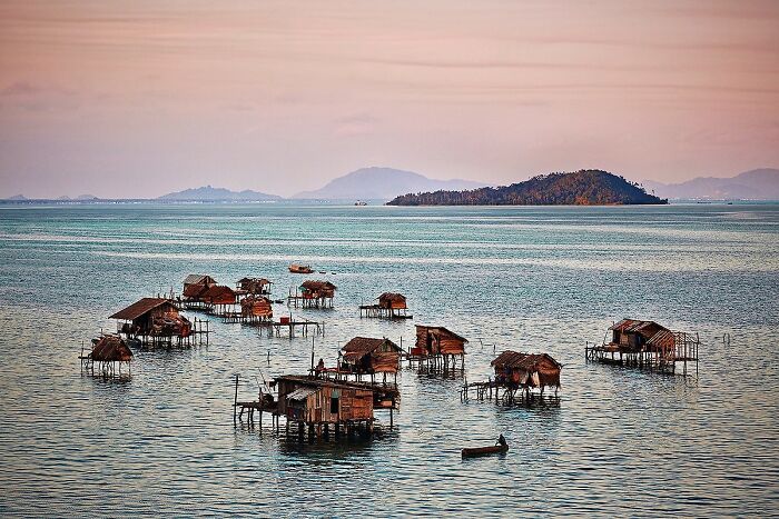 Houses on stilts over water at sunset, capturing global culture and tradition by Andrew Newey.