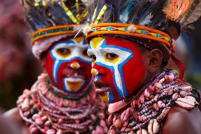 Two individuals in vibrant traditional attire and face paint, highlighting global culture and tradition.