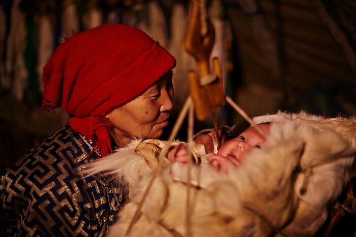 Elder woman in traditional attire tenderly watching over a baby in a cultural setting.