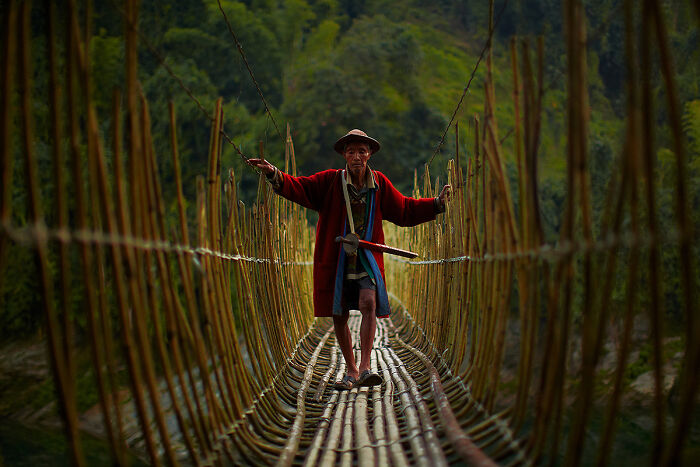 Man in traditional attire crossing a bamboo bridge, showcasing global culture and tradition.