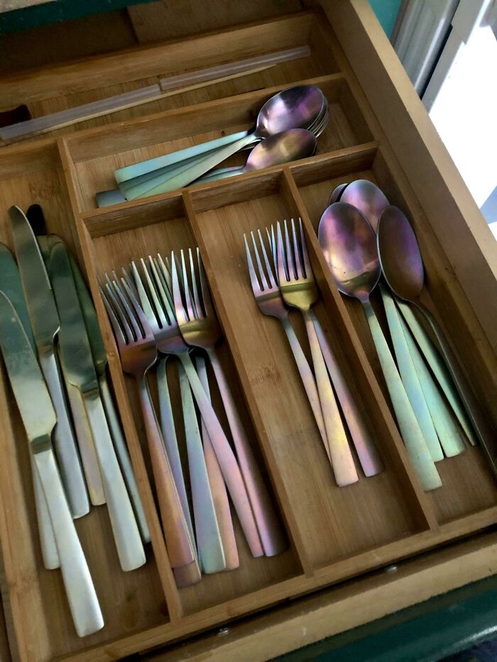 Drawer holding cutlery with iridescent wear, showcasing things used over time.