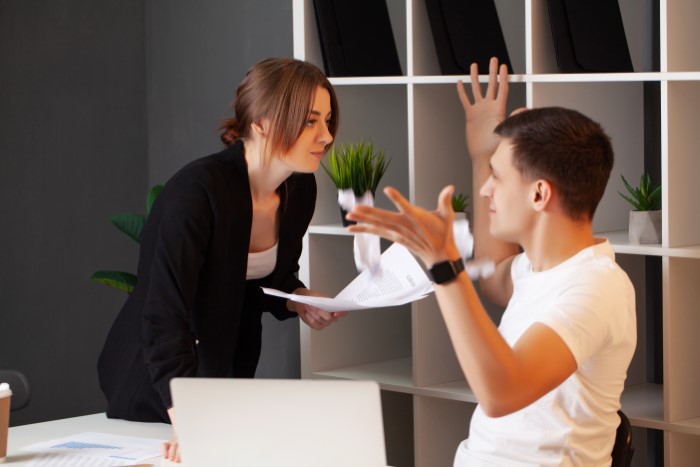 Employee confidently confronts boss, papers scattered, showcasing malicious compliance in a modern office setting.