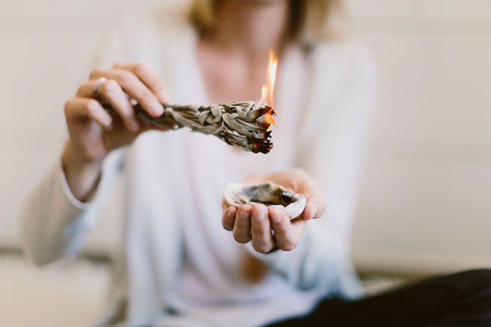 Person holding burning sage for home cleansing ritual indoors. Person holding burning sage for home cleansing ritual indoors.