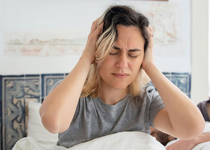 Night shift worker covering ears in frustration due to noise, seeking a peaceful morning.