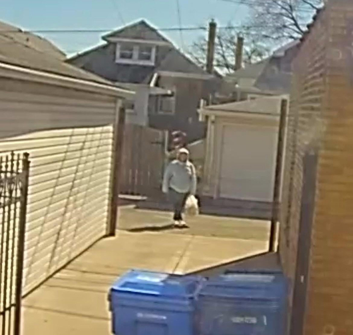 Woman in a residential alley, holding a bag, near garages and garbage bins, related to OCD and fence dispute.