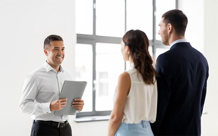 A man with a tablet is smiling at two people in a bright office, highlighting a discussion about moving to a blue state.