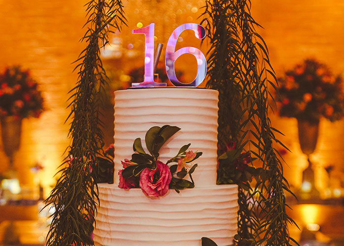 Sweet 16 cake adorned with pink flowers and a large "16" topper against a warm, festive backdrop.