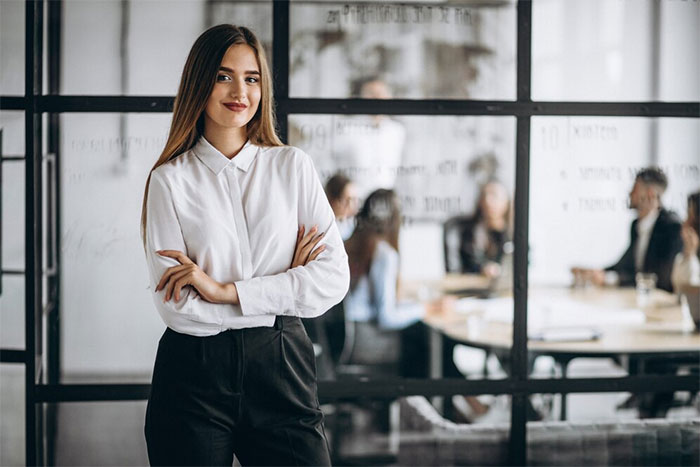 Confident woman in a white shirt standing in office, embodying malicious compliance in a modern workspace.