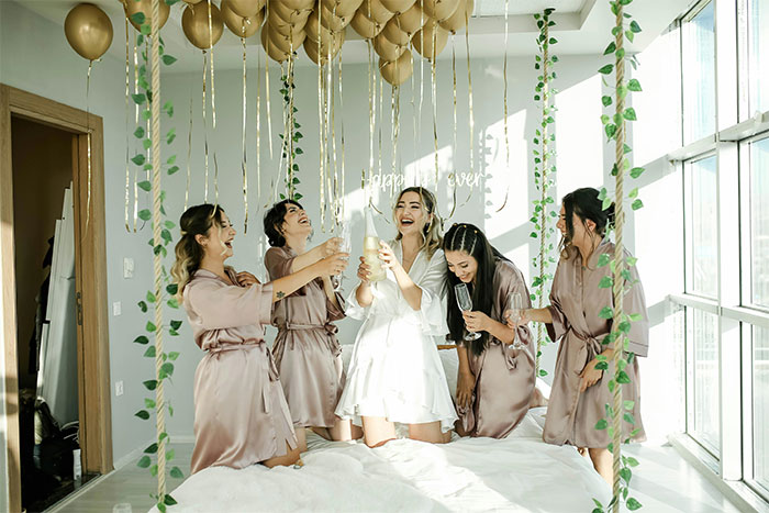 Women celebrating in a room with balloons, wearing robes, symbolizing bachelorette party festivities.