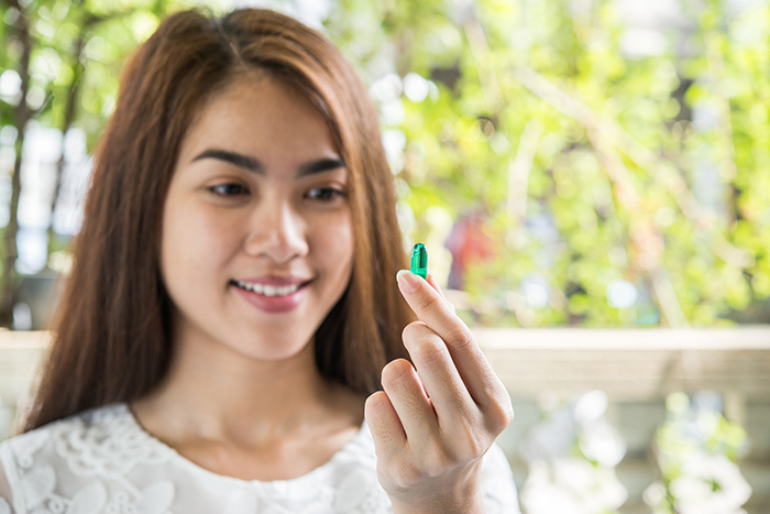 A woman holding a green capsule outdoors, relating to food spiked with laxatives.