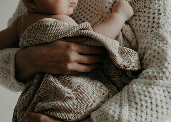 A person holding a baby wrapped in a knit blanket, symbolizing adoption and family decisions.