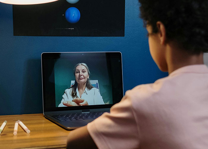 Child video chatting with a teacher on a laptop, discussing name pronunciation issues.