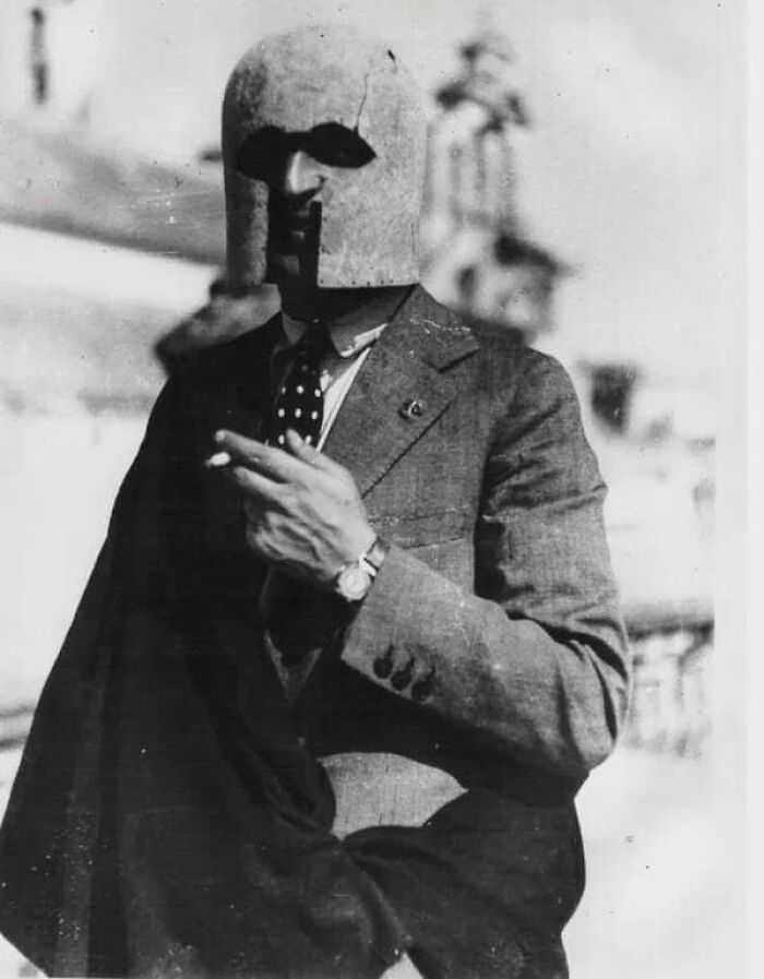 Man in a suit wearing a peculiar helmet, holding a cigarette in a forgotten corner of history.