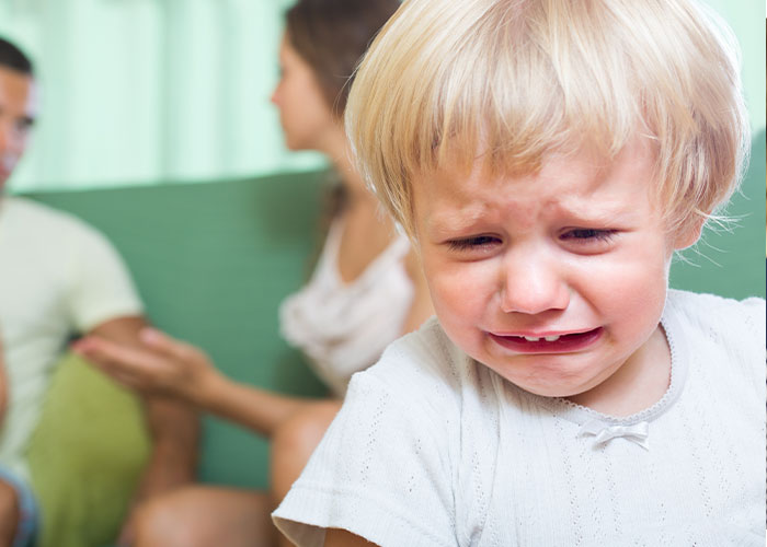 Crying child with upset parents in background, illustrating behaviors of a trashy parent.