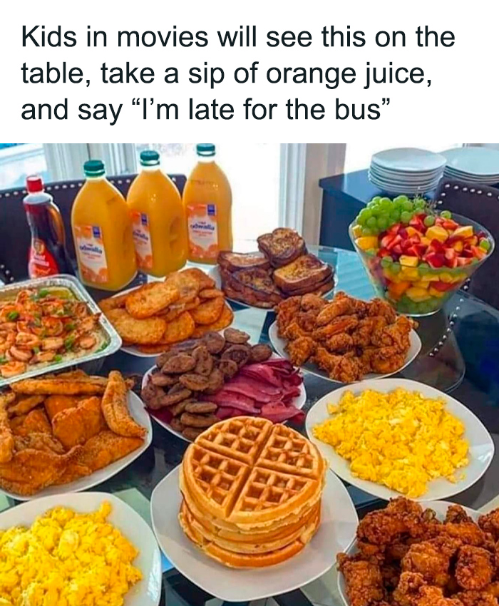 Unhinged food chaos: scrambled eggs, waffles, fried chicken, bacon, sausages, fruit salad, and orange juice on a table.