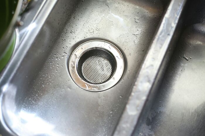 Clean stainless steel sink with water droplets and a cat-themed filter, showcasing unexpected cat gifts.
