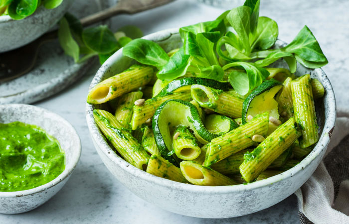 Bowl of lazy meal pasta with zucchini, fresh greens, and pesto sauce on the side.