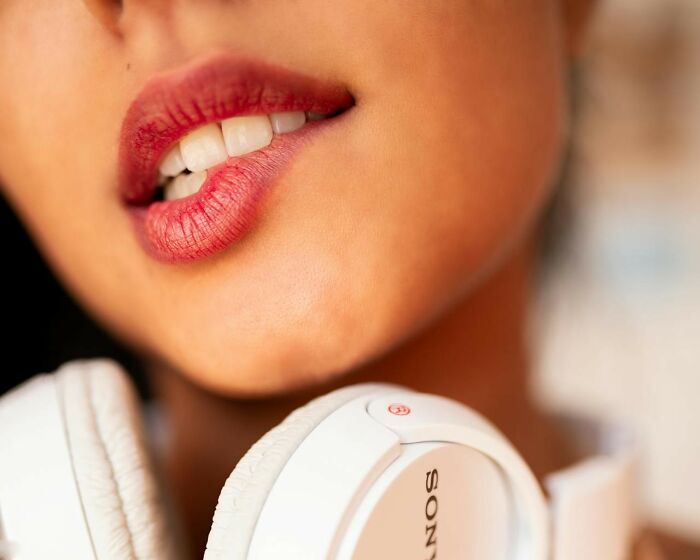 Close-up of a person biting their lip with Sony headphones, symbolizing hidden secrets and personal thoughts.