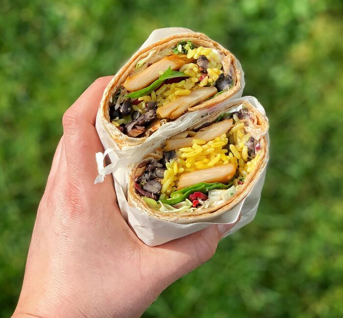 A hand holding a wrap filled with chicken, rice, and vegetables, symbolizing the concept of a lifetime supply.