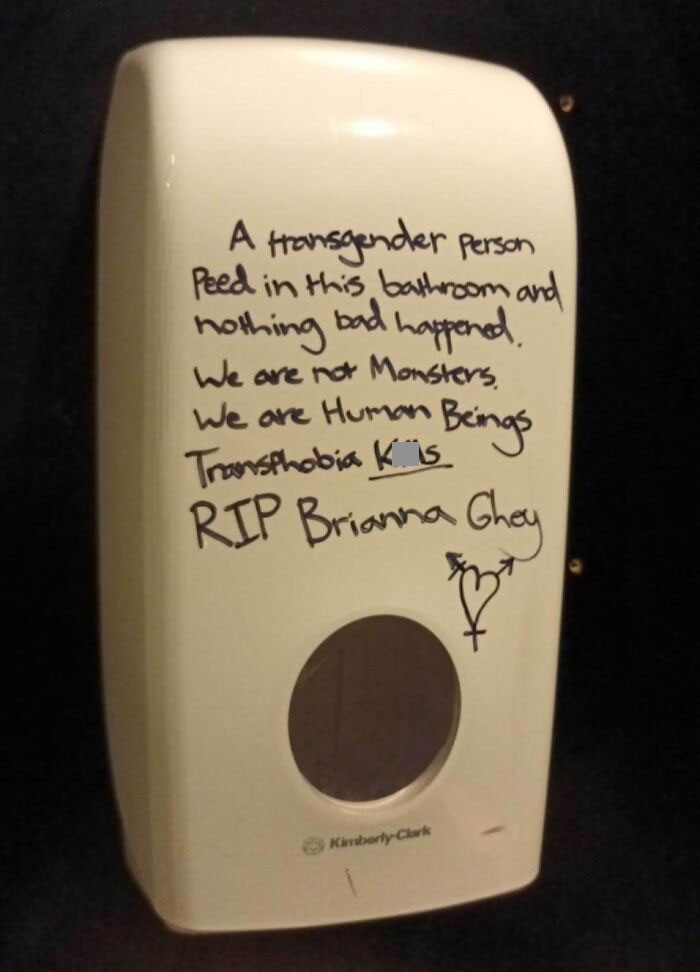 Public bathroom dispenser, supportive message against transphobia written on it, showing people having each other's backs online.