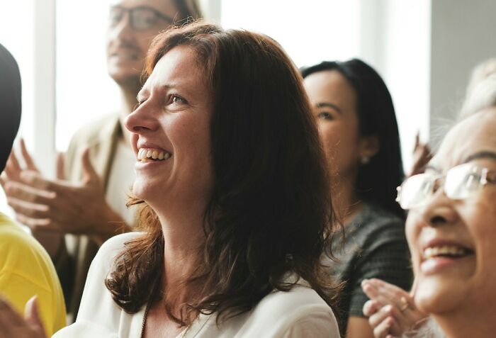 A woman smiling at a wedding event, surrounded by a cheerful crowd.