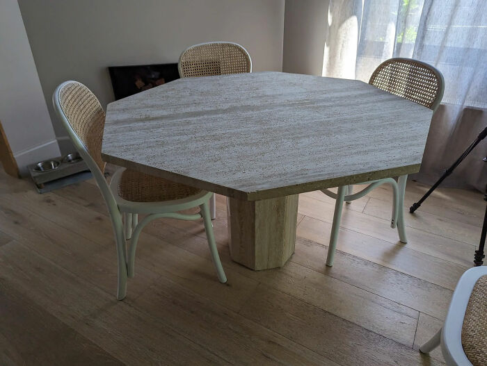 Octagonal stone dining table with rattan chairs in a poorly-aging interior design trend setting.