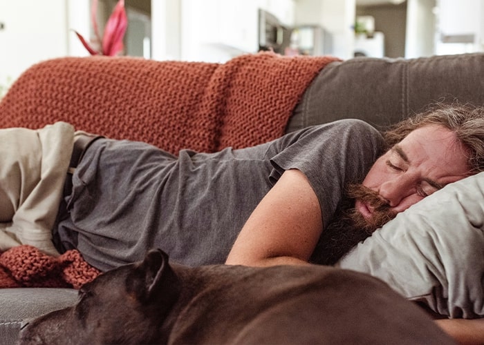 Man sleeping on a couch with a dog, illustrating parenting mistakes like letting exhaustion take over.