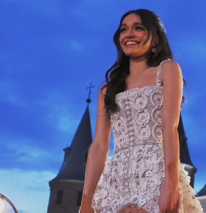 Young woman in a detailed white dress, smiling in front of castle-like towers at dusk, related to Snow White movie discussion.
