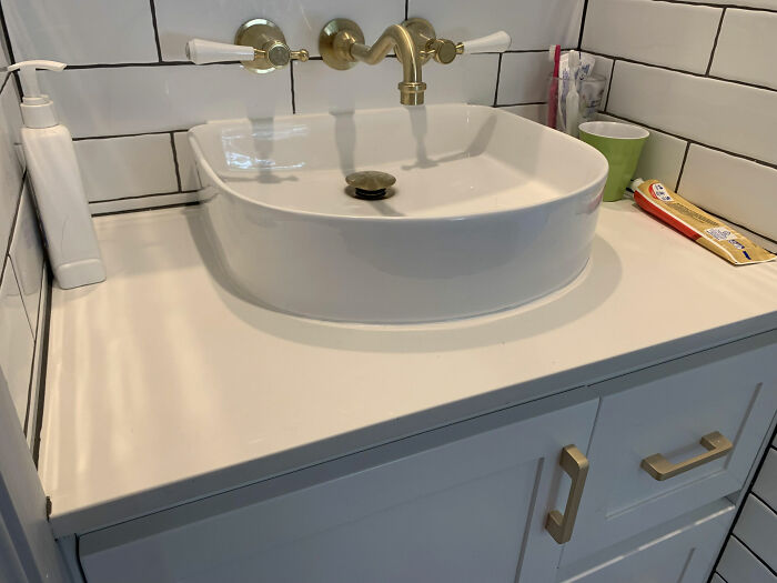 Modern bathroom sink with brass fixtures and white tiled walls, showcasing interior design trends to avoid.