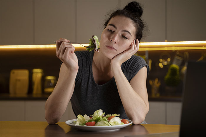Woman pondering a salad in a kitchen setting, questioning misunderstood "healthy" habits.