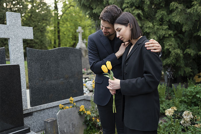 Two people in black holding yellow tulips at a grave, symbolizing honoring on an anniversary. Two people in black holding yellow tulips at a grave, symbolizing honoring on an anniversary.